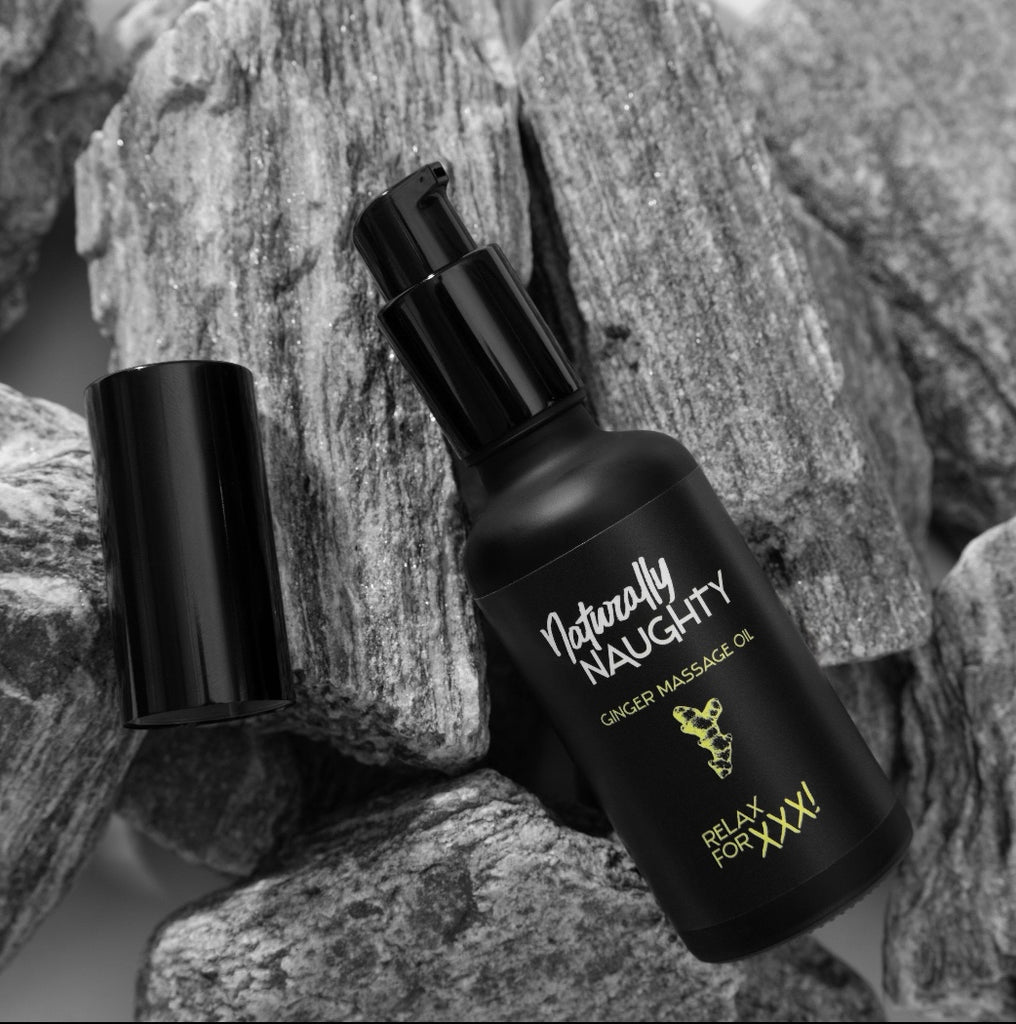 Flasche des 'Naturally Naughty Ginger Massage Oil' mit geöffnetem Deckel, liegend auf grauen Steinen, zur Darstellung eines natürlichen, sinnlichen Massageöls.