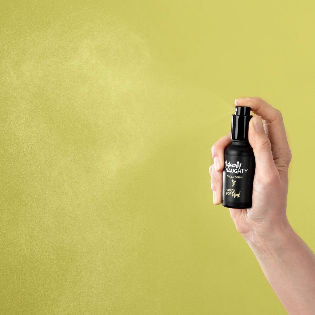 Hand sprüht Ingwer-Spray 'Naturally Naughty' in die Luft, gelber Hintergrund, Produktanwendung.